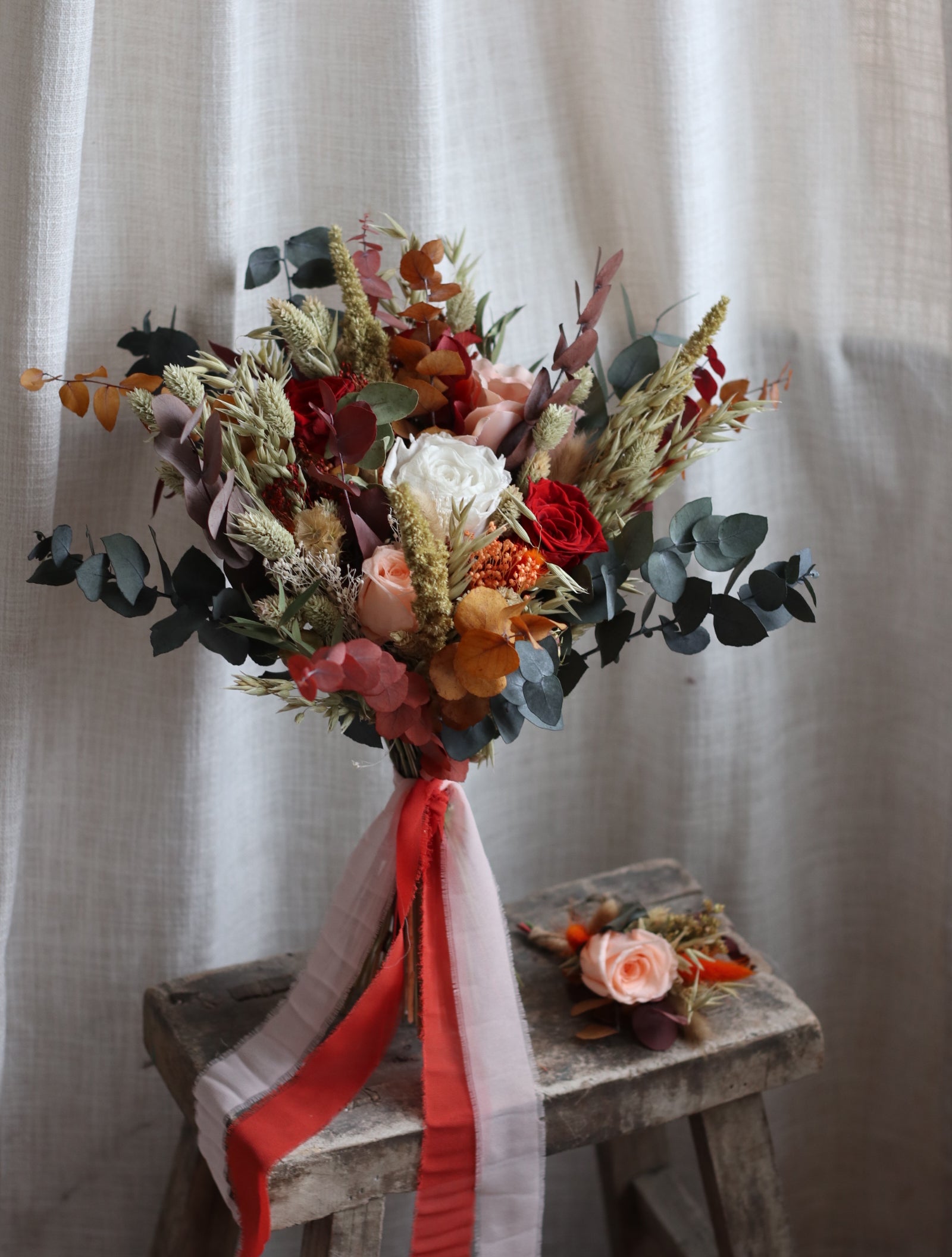 Bouquet of flowers with red and white ribbons on a wooden box against a white curtain background