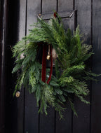 Green wreath with a red ribbon and gold bell on a black door