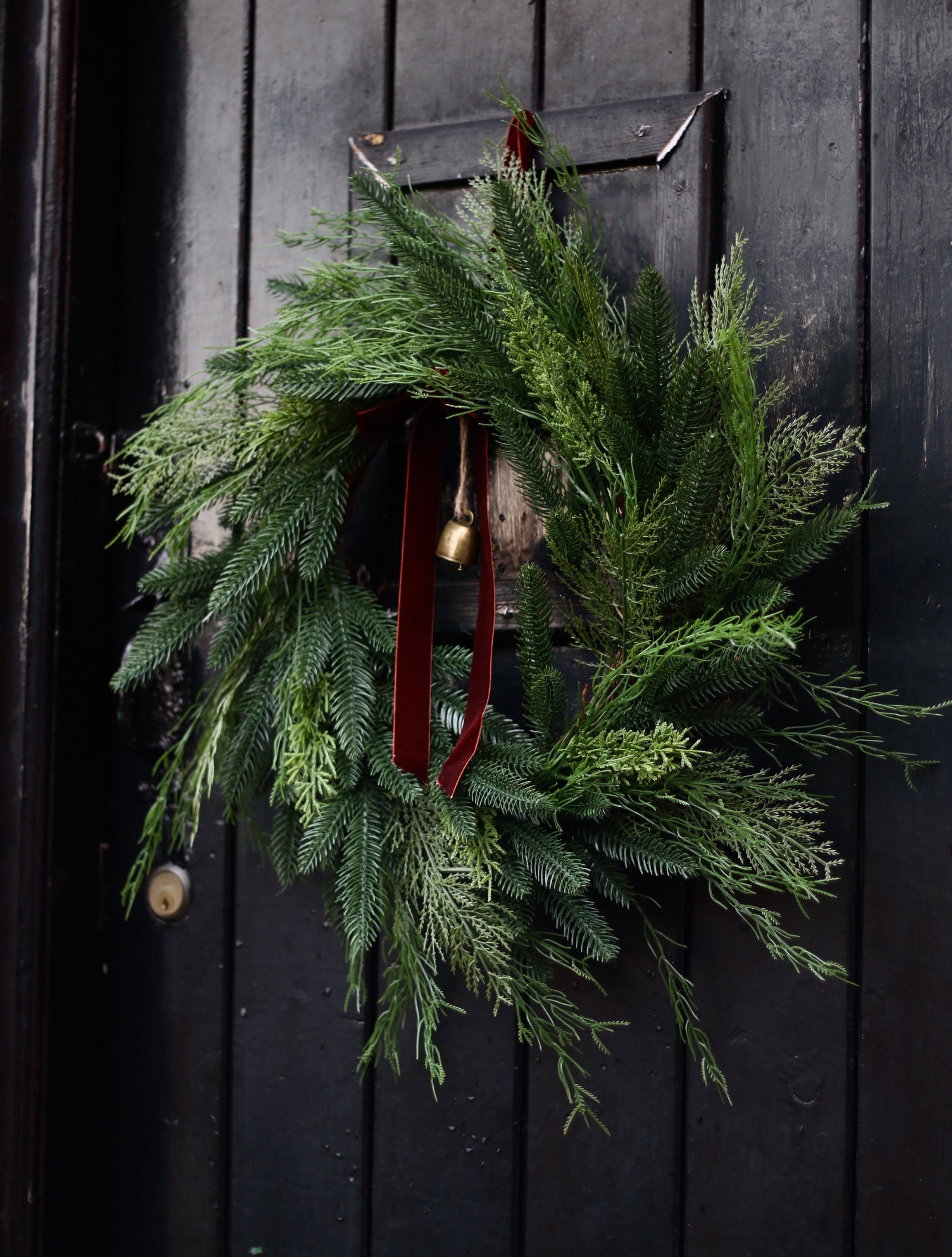 Green wreath with a red ribbon and gold bell on a black door