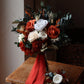 Bouquet of flowers with red and white ribbons on a wooden chair.