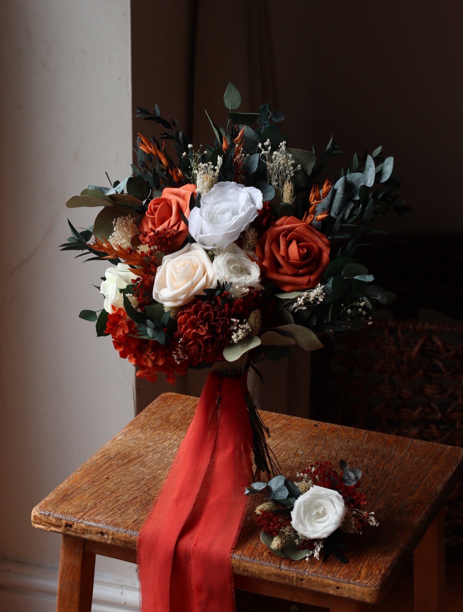 Bouquet of flowers with red and white ribbons on a wooden chair.