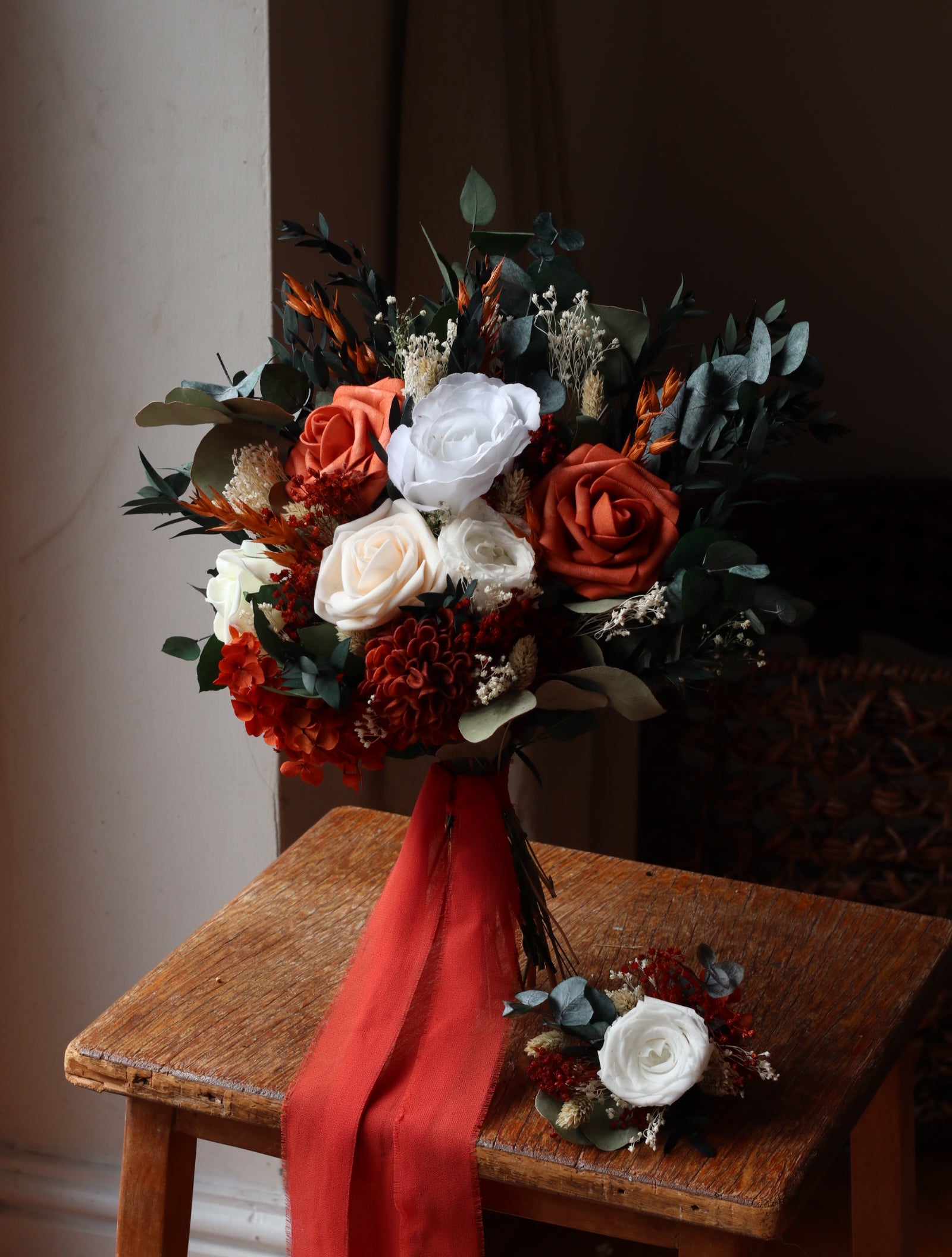 Bouquet of flowers with red and white ribbons on a wooden chair.