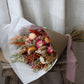 Bouquet of dried flowers wrapped in brown paper with a pink ribbon on a neutral background