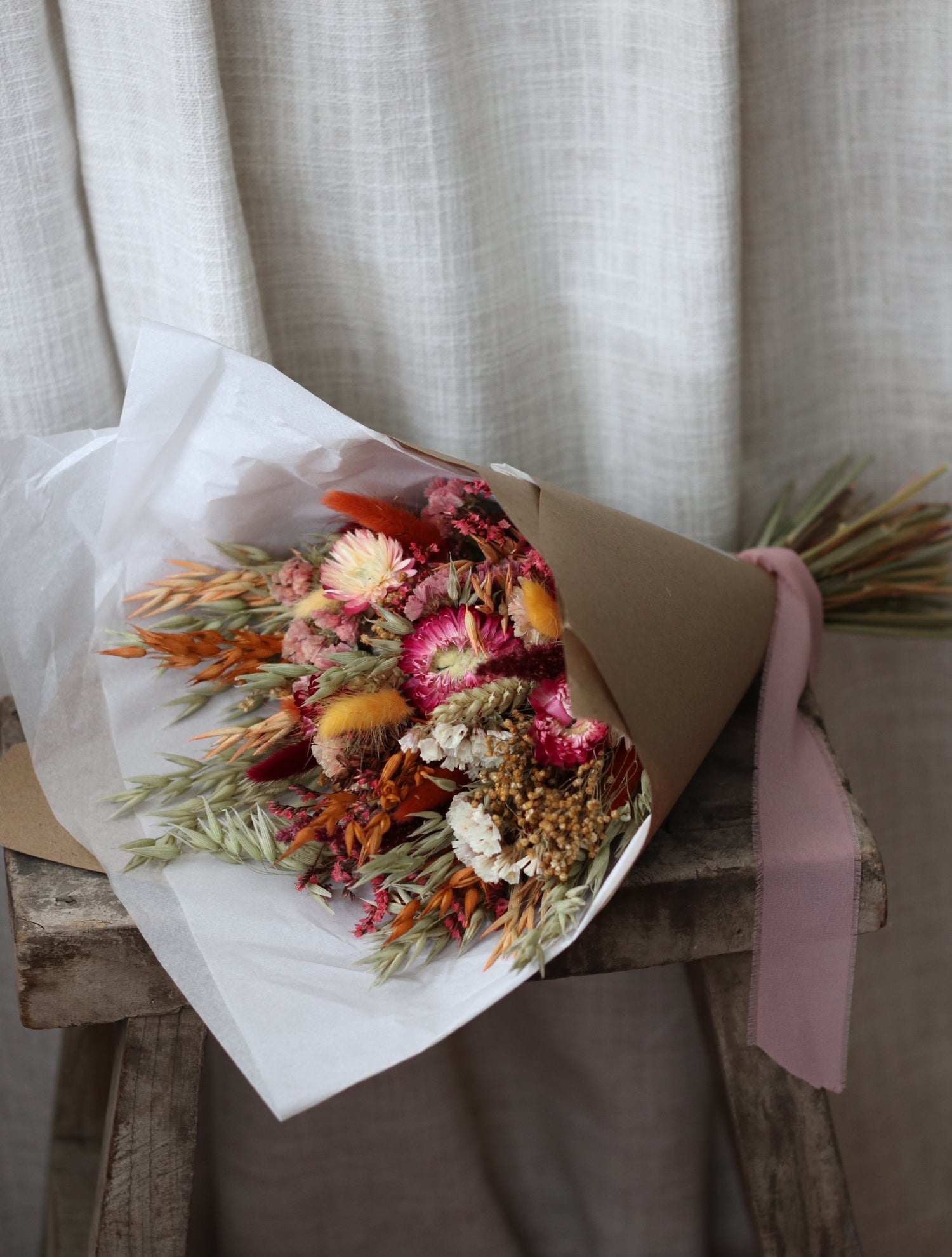 Bouquet of dried flowers wrapped in brown paper with a pink ribbon on a neutral background