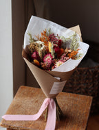 Bouquet of dried flowers wrapped in brown paper with a pink ribbon on a textured surface.