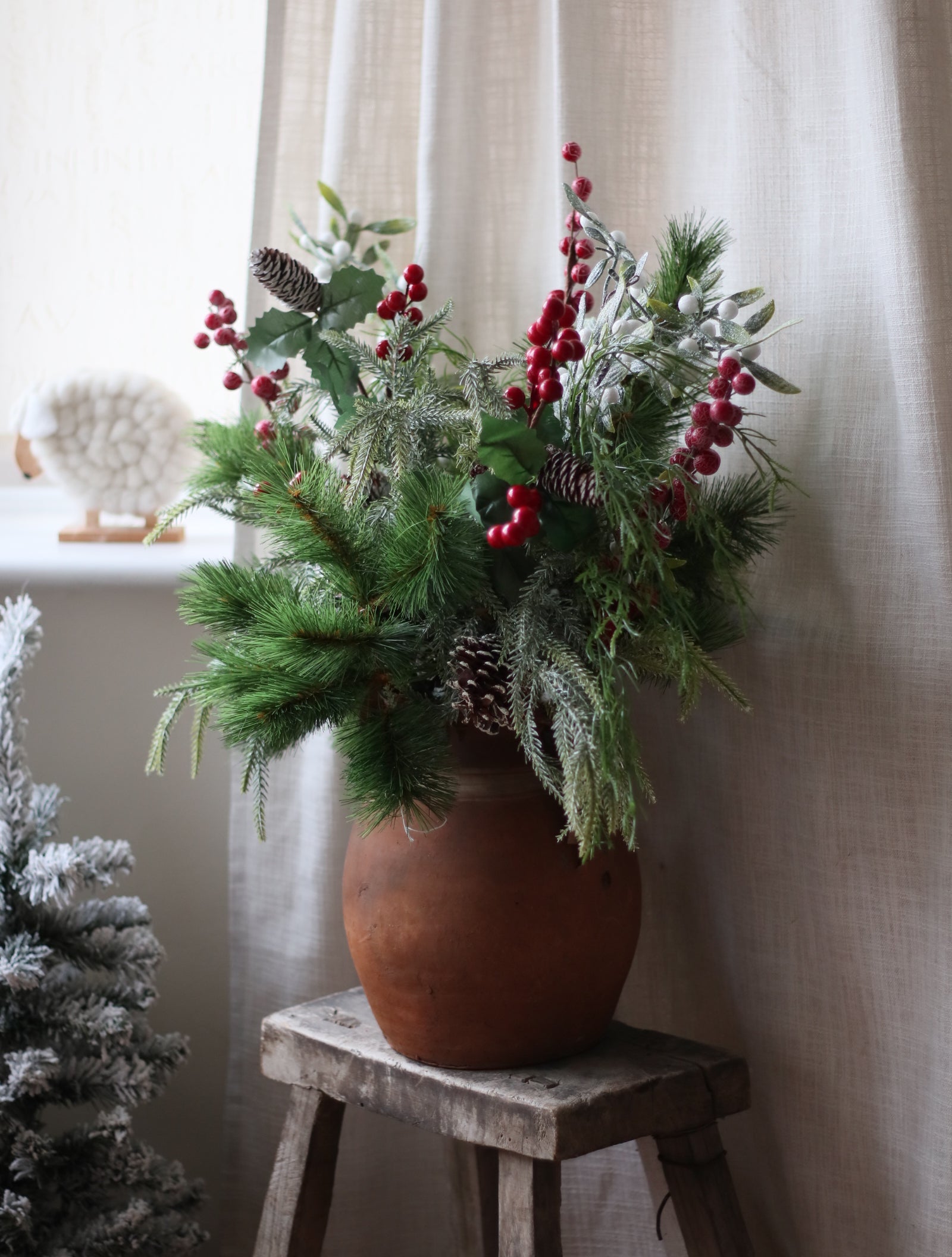 Decorative arrangement of greenery with red berries on a windowsill.
