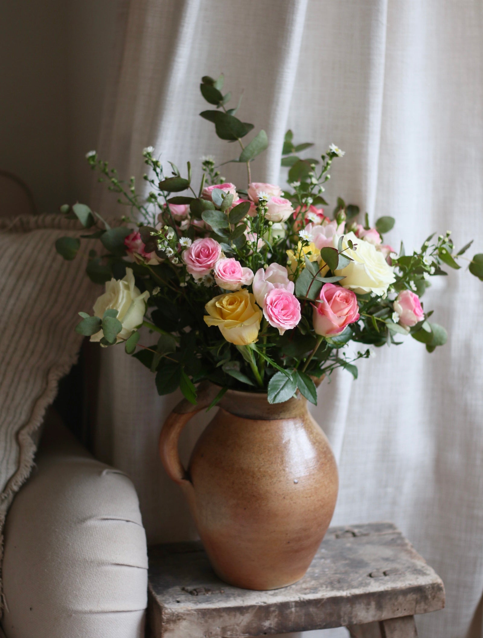 Bouquet of flowers in a vase on a wooden stool with a soft, neutral background