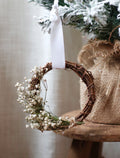 Small wreath with baby's breath flowers hanging on a snowy branch.