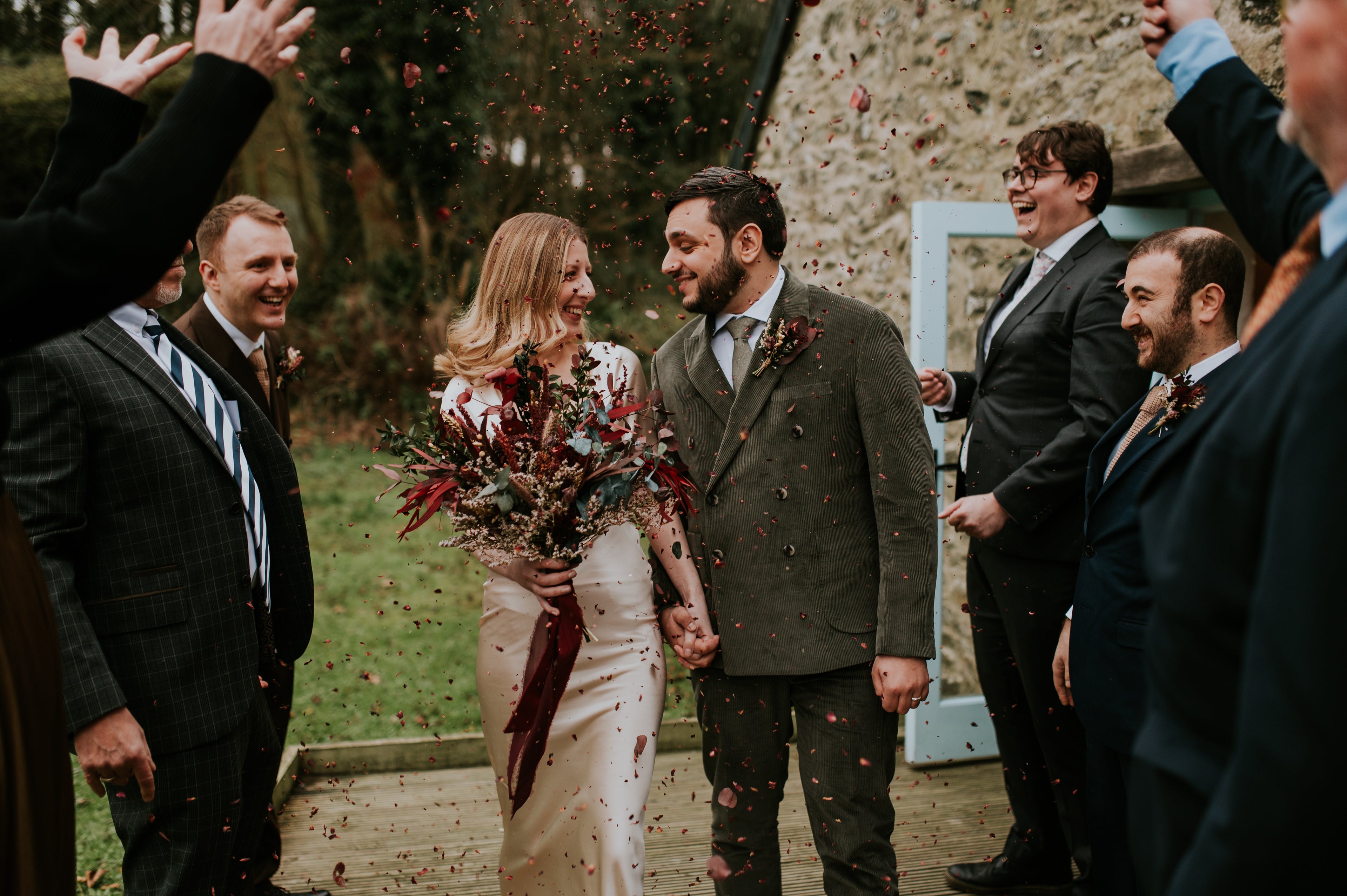 Wedding couple walking through a line of guests with confetti, outdoors. holding an autumn dried flower bouquet