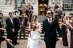 Wedding couple walking down steps  holding a dried flower bouquet with guests clapping, wearing sunglasses.