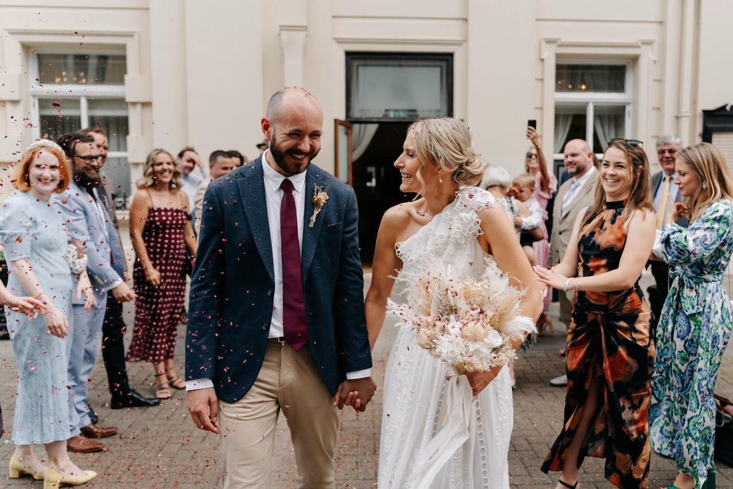 Wedding couple walking through a crowd of guests outdoors. with a dried flower bouquet
